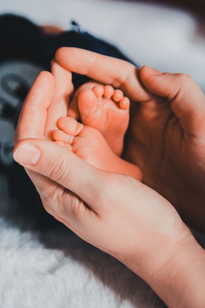 A close-up of a mother's hands gently holding her newborn's tiny feet, symbolizing care and love.
