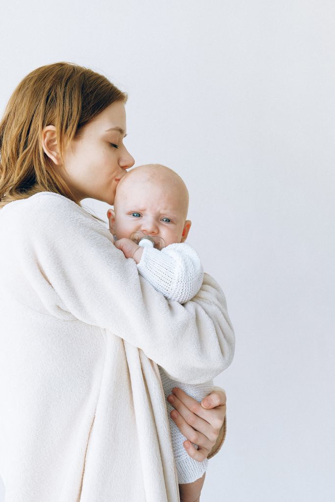 Loving mother gently kisses her calm baby wrapped in a warm sweater.